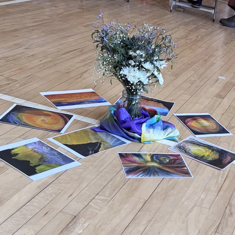Obras en pastel dispuestas en círculo en el suelo de una sala, alrededor de un ramo de flores