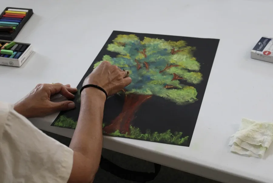 Manos de una participante trabajando un dibujo de un árbol en pastel